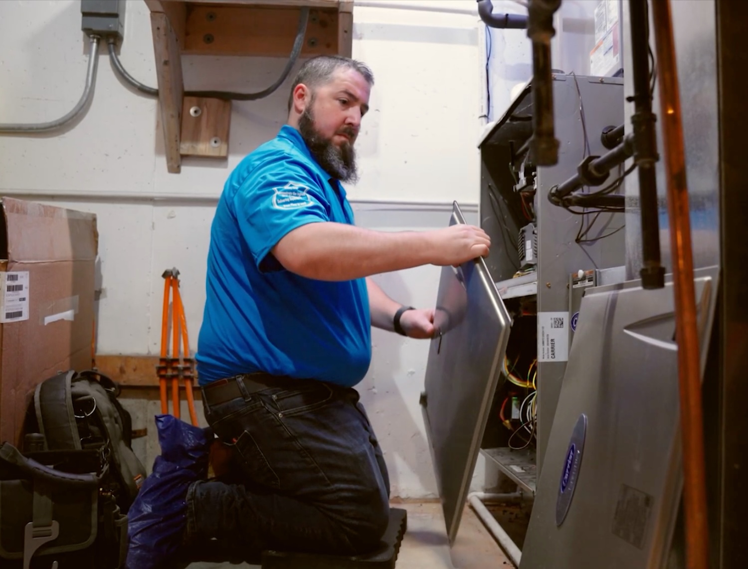 Technician servicing HVAC system in utility room, kneeling and inspecting internal components for maintenance.