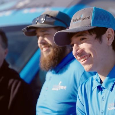 Employees in blue uniforms smiling, standing outdoors with a branded vehicle in the background.