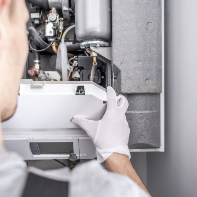 Technician servicing boiler with gloves on, inspecting internal components for maintenance and efficiency.