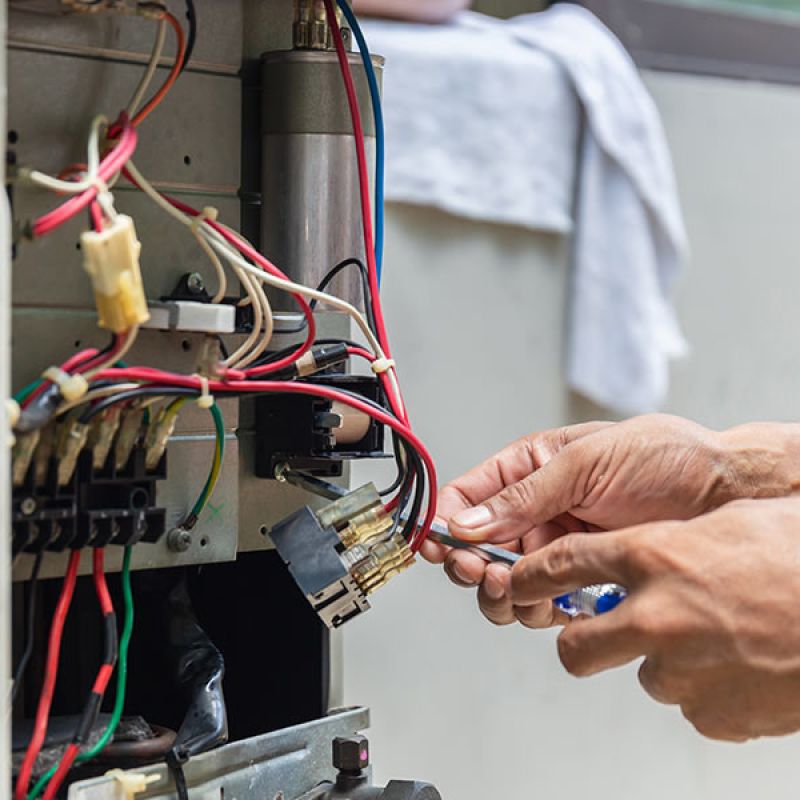 Hands repairing an HVAC unit with wires exposed, showcasing maintenance work and expertise.