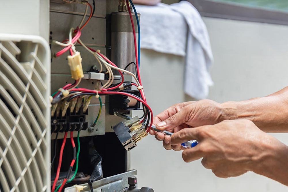 Hands repairing an HVAC unit with wires exposed, showcasing maintenance work and expertise.