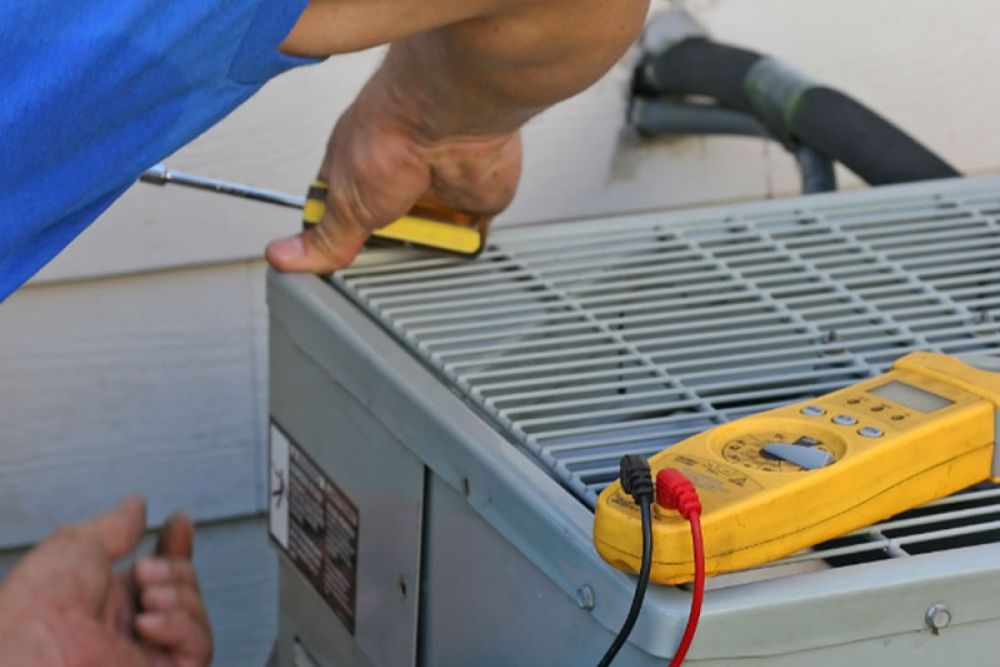 Technician fixing air conditioner with screwdriver, multimeter on unit for maintenance check.