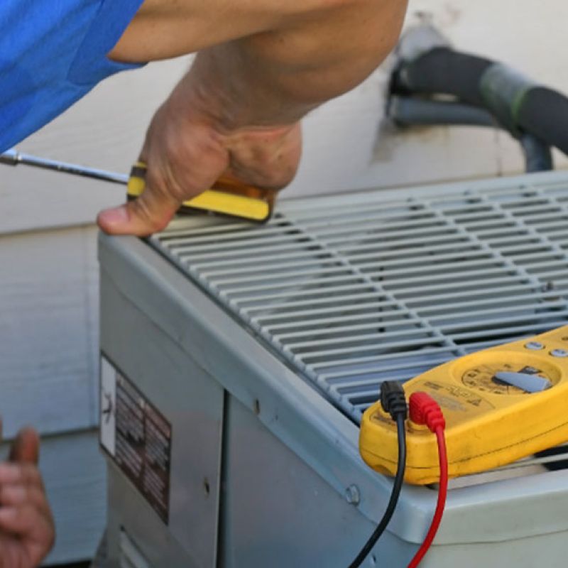 Technician fixing air conditioner with screwdriver, multimeter on unit for maintenance check.