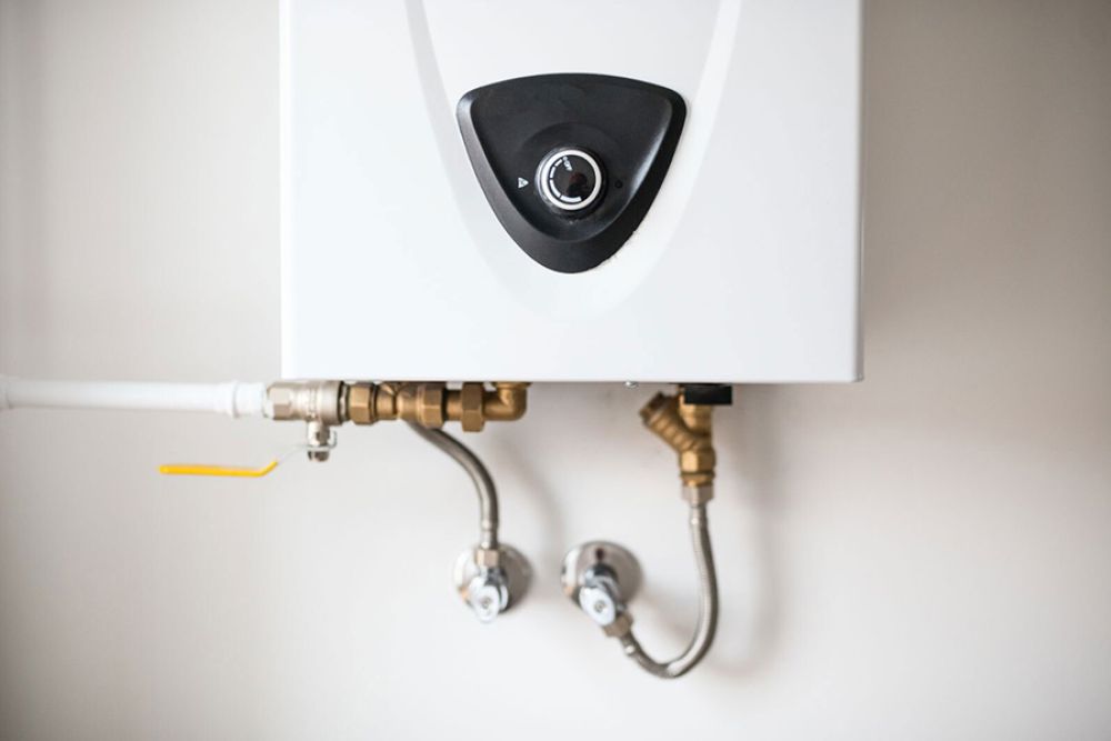 Close-up of a white tankless water heater mounted on a wall with visible pipes and connections.