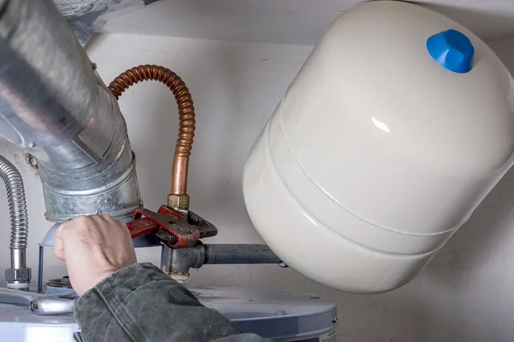 Person adjusting water heater expansion tank with wrench in home basement.