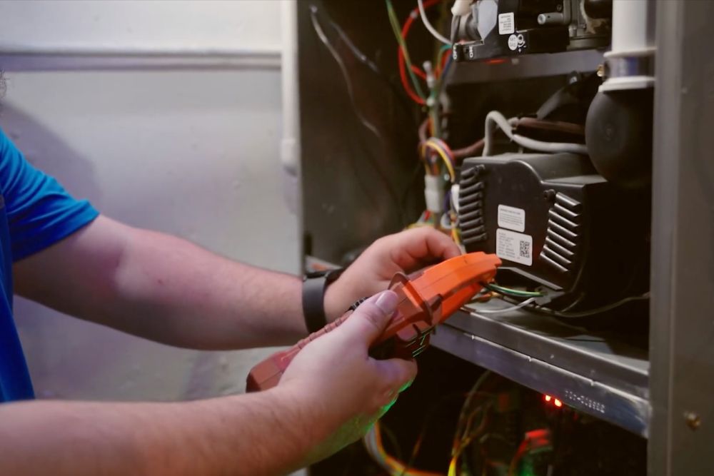 Technician using a multimeter to inspect HVAC wiring inside a panel for maintenance and troubleshooting.