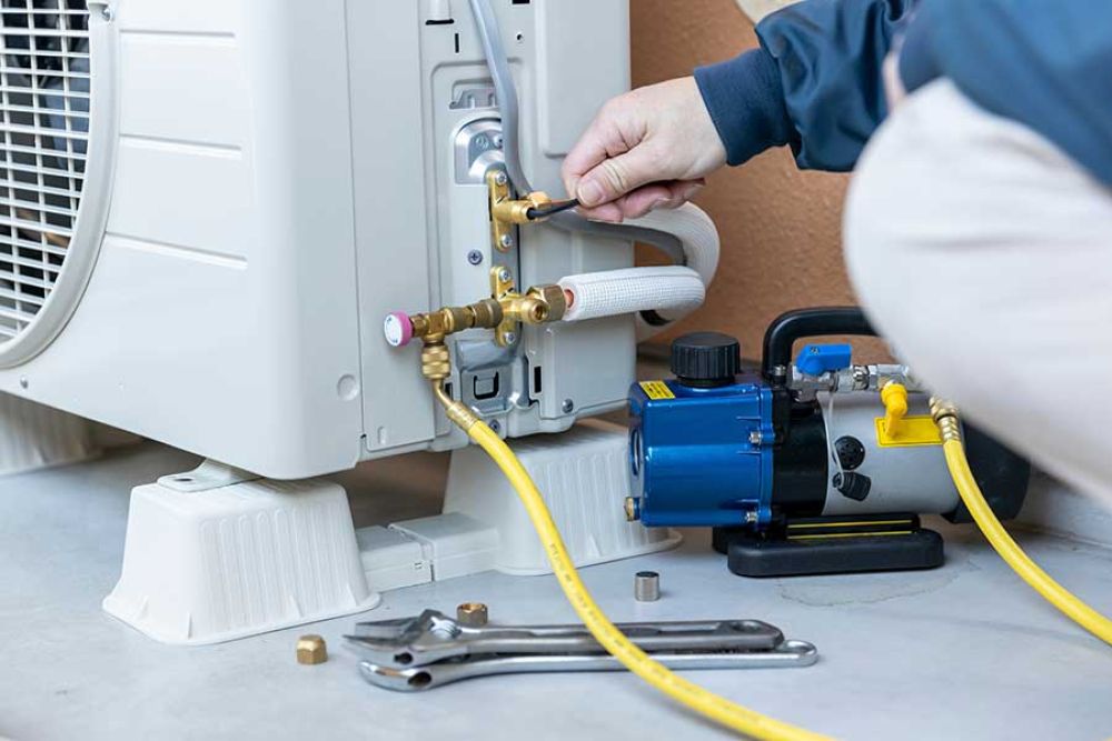 Technician servicing air conditioner unit with tools and yellow hose.