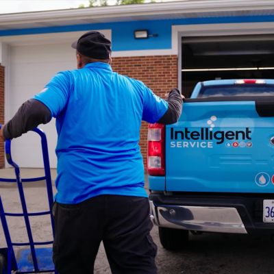 Worker with hand truck beside Intelligent Service truck outside a brick building. Illinois license plate visible.