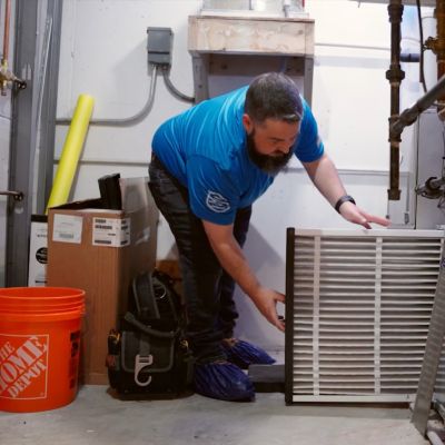 Technician replacing HVAC filter in utility room next to tools and supplies, ensuring efficient air conditioning.