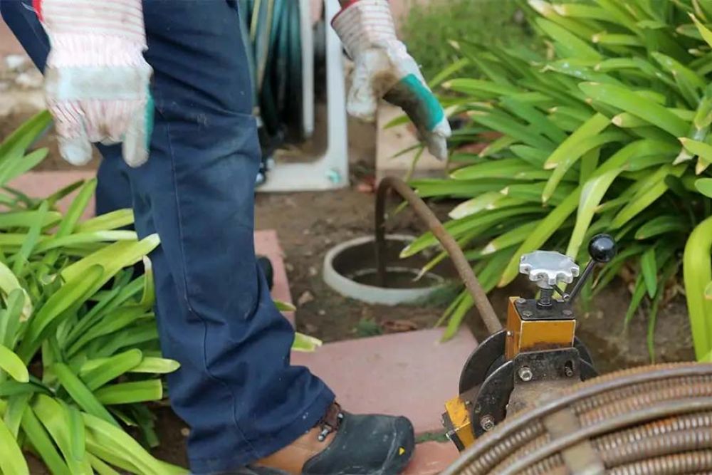 Worker using drain cleaning machine in garden area for plumbing maintenance.