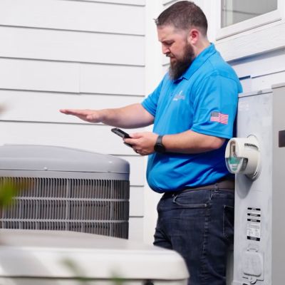 Technician inspecting HVAC unit with smartphone outside a house.