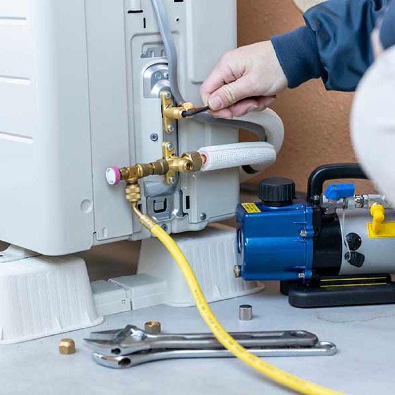 Technician servicing air conditioner unit with tools and yellow hose.