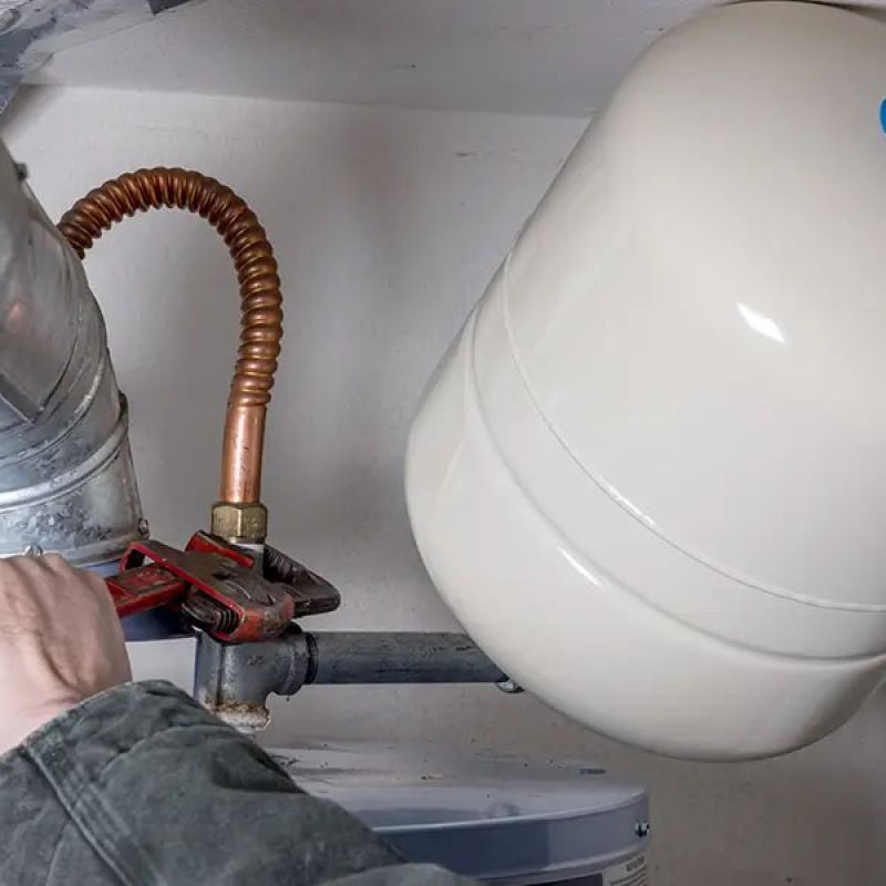 Person adjusting water heater expansion tank with wrench in home basement.