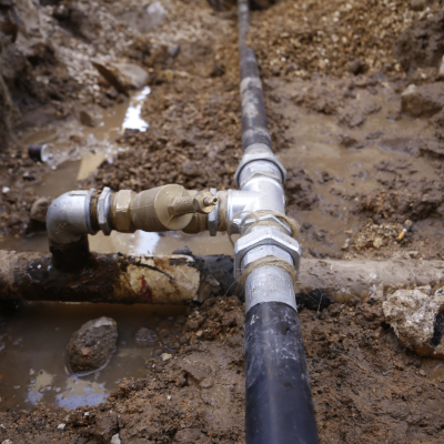 Buried plumbing pipeline system with metal joints and valves in a muddy trench.