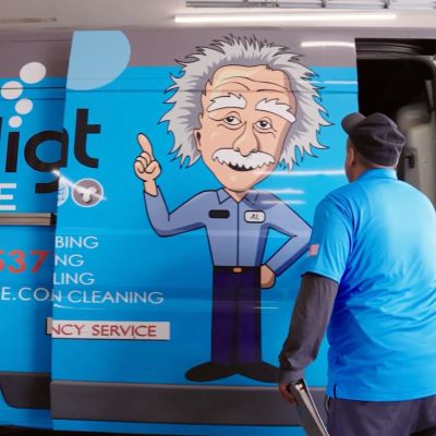 Technician standing by a blue van with Einstein cartoon, branded with Intelligent Service and contact details.