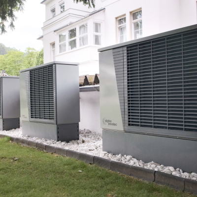 Outdoor heat pumps installed by a building, surrounded by greenery for energy-efficient heating solutions.