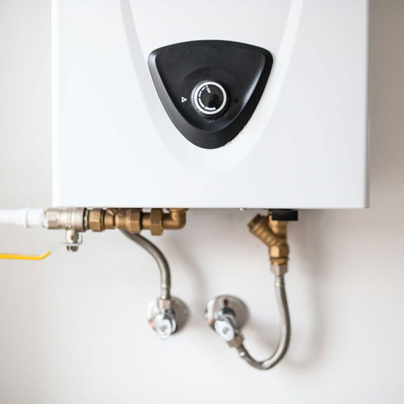 Close-up of a white tankless water heater mounted on a wall with visible pipes and connections.